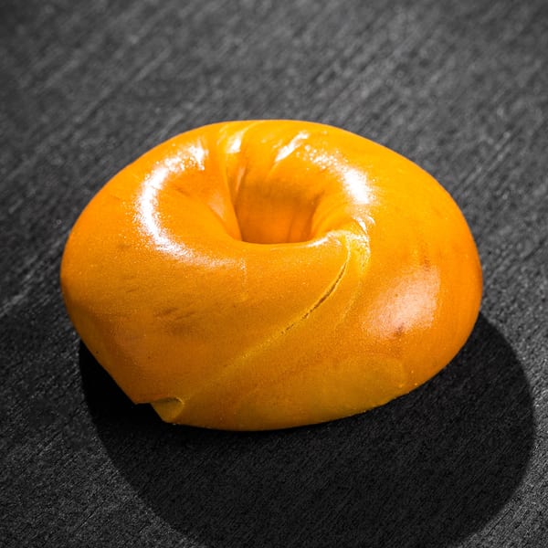 A golden-brown bagel with a shiny crust sits on a dark, textured surface.