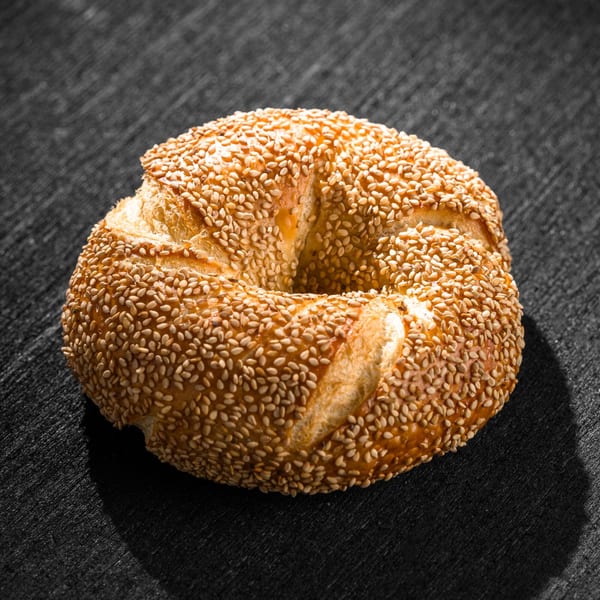 A golden-brown Go Bagels sesame bagel, perfectly baked, rests on a dark textured surface.