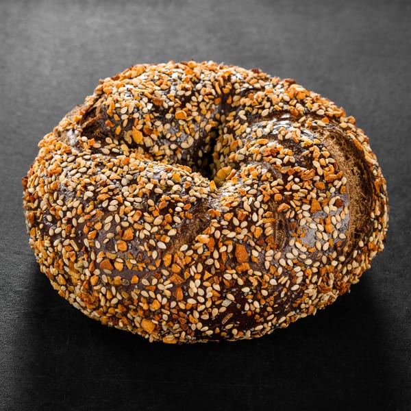 Dark bagel with a generous topping of sesame seeds and crispy garlic bits on a black surface.
