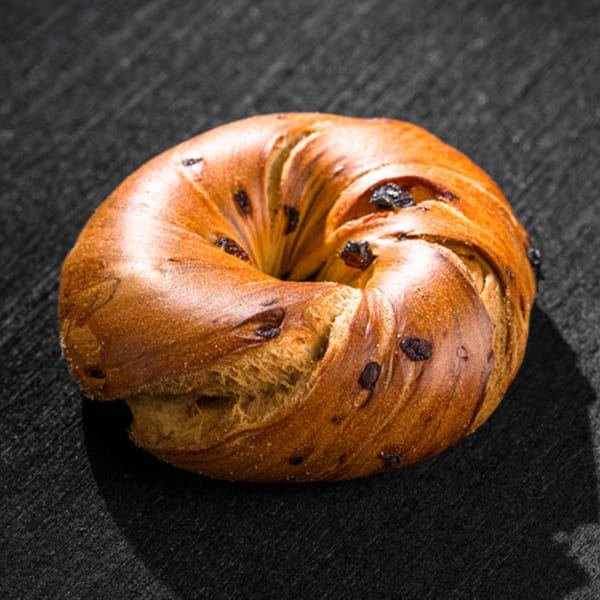A golden-brown cinnamon raisin bagel from Go Bagels, with visible raisins and a textured surface.