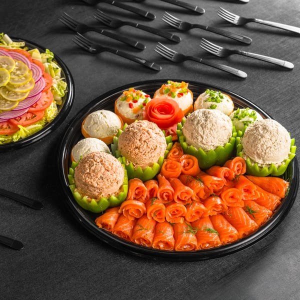A catering platter with various cream cheese scoops, rolled salmon, and a side salad.