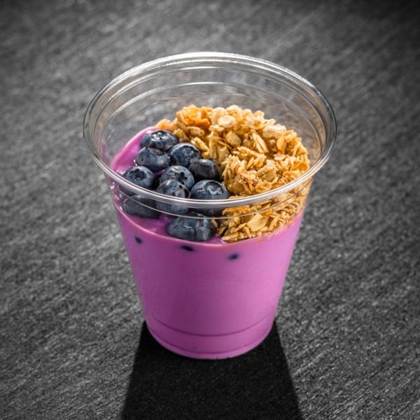 A vibrant purple smoothie bowl with blueberries and granola in a clear plastic cup.