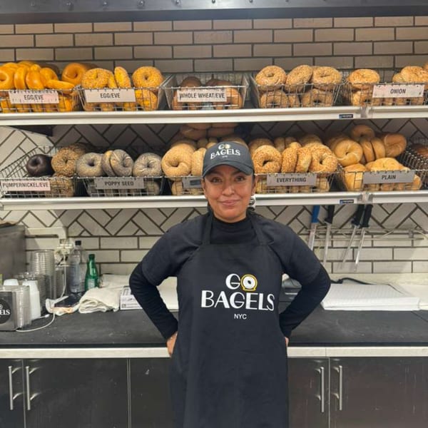 A Go Bagels NYC employee smiles in front of shelves filled with various bagels.