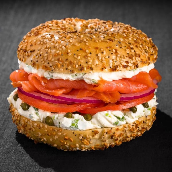 Everything bagel with lox, cream cheese, red onion, tomato, and capers on a dark surface.