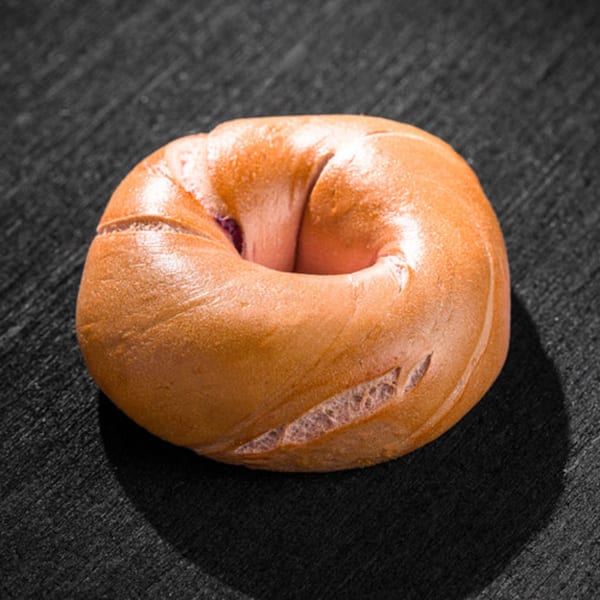 A golden-brown Go Bagels bagel with a slightly cracked surface rests on a dark background.