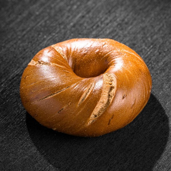 A single, golden-brown Go Bagels bagel with a shiny crust rests on a dark, textured surface.