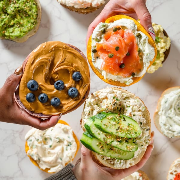 Hands hold Go Bagels with peanut butter and blueberries, lox and capers, and cucumber with everything seasoning.