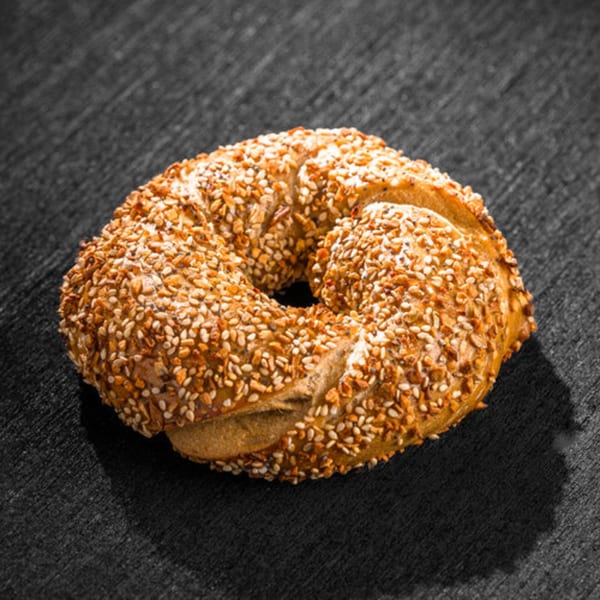 A golden-brown Go Bagels bagel, generously covered in sesame seeds and poppy seeds, on a dark surface.