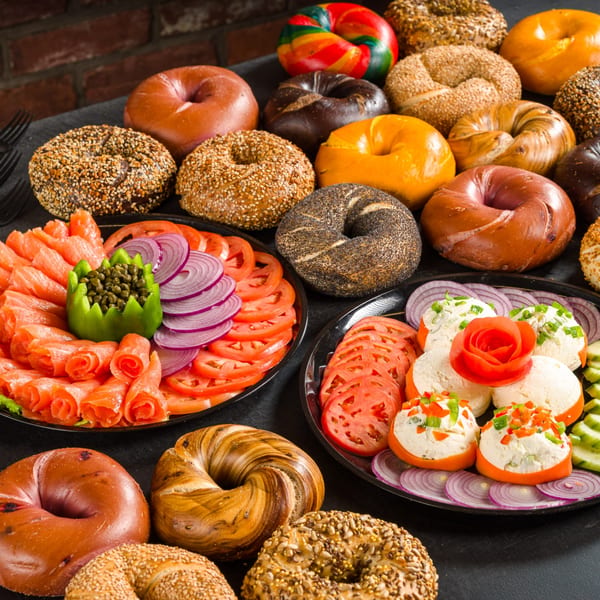 A large spread of Go Bagels with various toppings, lox, cream cheese, and vegetables.