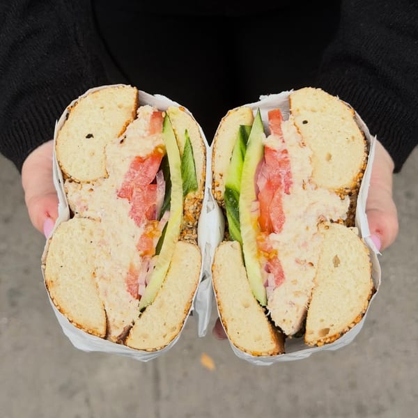 Hands holding a Go Bagels everything bagel sandwich, cut in half, filled with cream cheese, tomato, and cucumber.