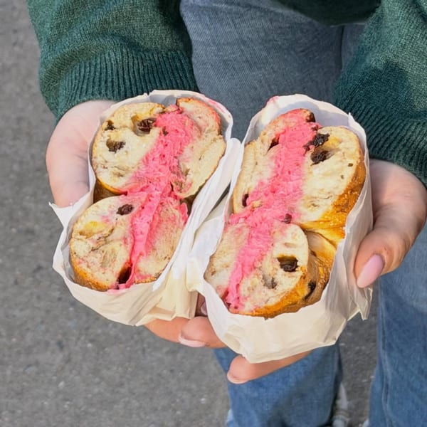 Hands holding two halves of a Go Bagels cinnamon raisin bagel with bright pink cream cheese.
