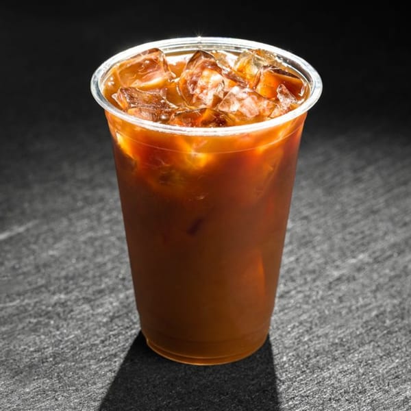 Iced coffee in a clear plastic cup with ice cubes, on a dark textured surface.