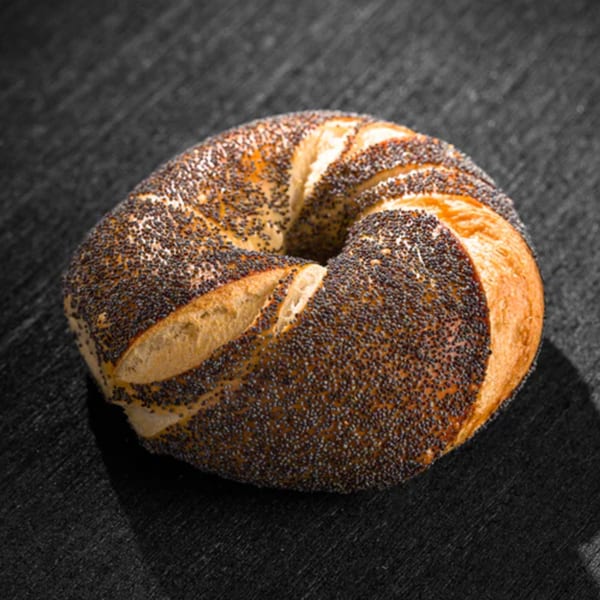 A Go Bagels poppy seed bagel, golden brown and sprinkled with seeds, rests on a dark surface.