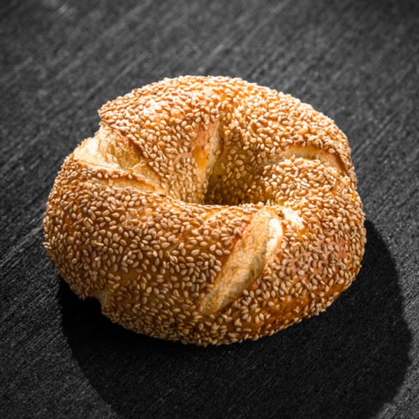 A golden-brown Go Bagels sesame bagel, perfectly baked, rests on a dark textured surface.