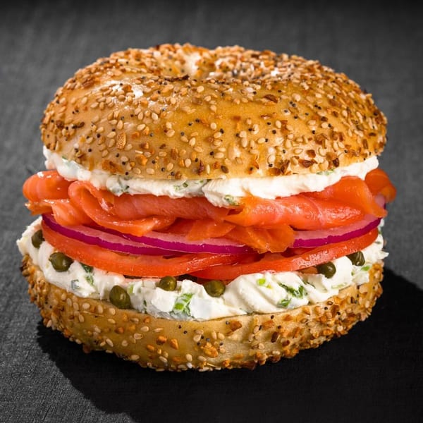 Everything bagel with lox, cream cheese, red onion, tomato, and capers on a dark surface.