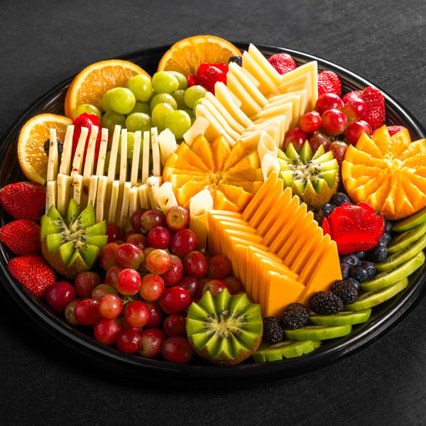A platter of sliced oranges, kiwi, grapes, strawberries, blueberries, and cheese sticks.