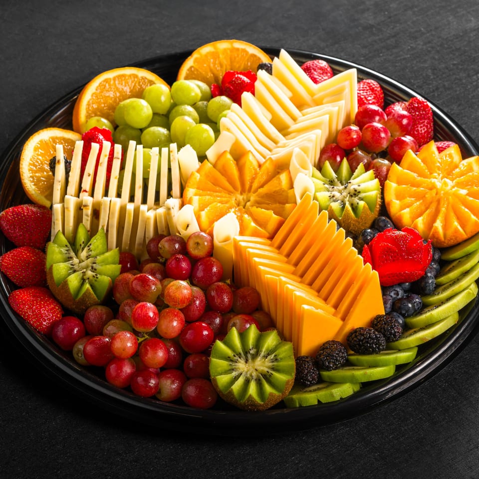 A platter of sliced oranges, kiwi, grapes, strawberries, blueberries, and cheese sticks.