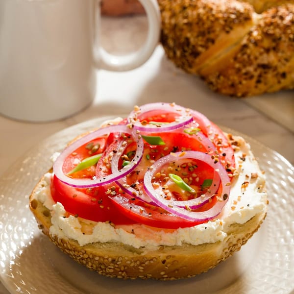 A Go Bagels sesame bagel with cream cheese, sliced tomatoes, red onion, and everything seasoning.