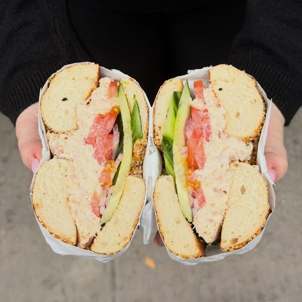 Hands holding a Go Bagels sandwich, cut in half, filled with cream cheese, tomatoes, and cucumbers.